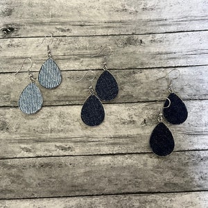 May include: Three pairs of denim teardrop earrings. The earrings are silver with a denim fabric covering the teardrop shape. One pair is light blue denim, one pair is dark blue denim, and one pair is black denim.