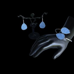 May include: A set of denim earrings and a denim bracelet. The earrings are teardrop shaped and the bracelet is a simple bangle with two denim teardrops attached.