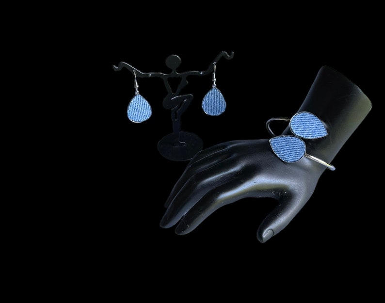 May include: A set of denim earrings and a denim bracelet. The earrings are teardrop shaped and the bracelet is a simple bangle with two denim teardrops attached.