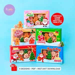 May include: Five rectangular Christmas cookie boxes with clear windows, featuring colorful illustrations of Santa Claus, gingerbread men, Christmas trees, and snowflakes. The boxes display text including Feliz Navidad and Merry Christmas.