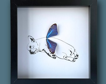 Pode incluir: Uma impressão emoldurada em preto de uma ilustração estilizada de um cão com uma borboleta nas costas. O cão está deitado de lado com as pernas esticadas. A borboleta é azul e roxa com veias pretas.