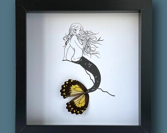 Pode incluir: Uma impressão emoldurada em preto de uma sereia com uma cauda de borboleta amarela e preta. A sereia é desenhada em tinta preta em papel branco.