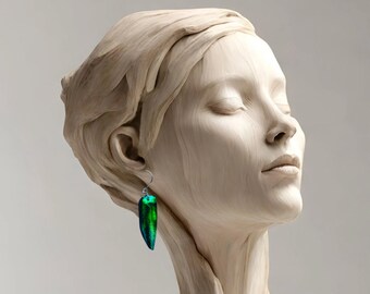 Pode incluir: Uma escultura de madeira de uma cabeça de mulher com os olhos fechados. Ela está usando um par de brincos longos, verdes e azuis.