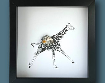 Pode incluir: Uma imagem emoldurada em preto com fundo branco que apresenta um recorte de papel em preto e branco de uma girafa correndo com um pequeno recorte de papel laranja e branco de um peixe nas costas.