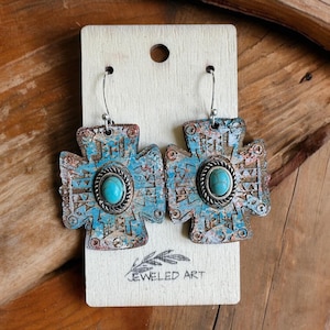 Puede incluir: Un par de pendientes de cruz turquesa y plata con un acabado desgastado. Los pendientes están en una tarjeta blanca con el texto "JEWELED ART".