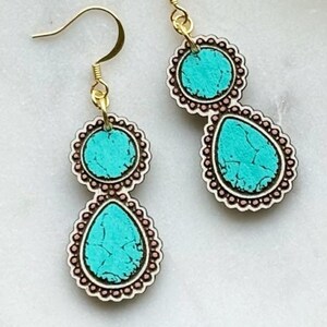 May include: A pair of gold-colored dangle earrings. Each earring features two turquoise-colored, teardrop-shaped and circular pendants with a decorative border. The earrings have a gold-colored fish hook closure.