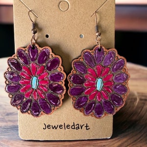 Könnte beinhalten: Ein Paar violette und rosafarbene Blumenohrringe mit einem türkisfarbenen Zentrum. Die Ohrringe sind aus Holz und haben einen Haken aus Kupferdraht.