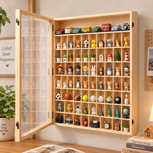 May include: A light-colored wooden display case with a hinged glass door, featuring multiple rectangular compartments filled with various miniature figurines, including toy cars, animals, sports balls, landmarks, and small household objects.