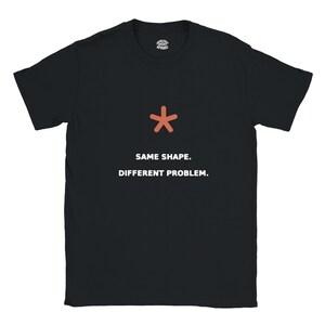 May include: A black short-sleeved t-shirt featuring an orange asterisk symbol positioned above the white text which reads SAME SHAPE. DIFFERENT PROBLEM. The garment includes a small circular logo on the inside neck area with the text ABSOLUTELY RIGHT APPAREL.