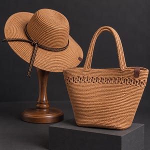 Op de afbeelding: Een beige hoed van gevlochten stro met een donkerbruine koordband en een bijpassende beige tas van gevlochten stro met een decoratieve gevlochten rand aan de bovenkant en twee stevige handvatten, beide met een consistente textuur.