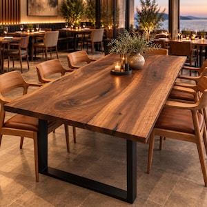 May include: A large rectangular dining table featuring a natural live-edge walnut wood top with visible grain patterns, supported by a sturdy black metal U-shaped frame base, accompanied by six wooden armchairs with brown leather seats.