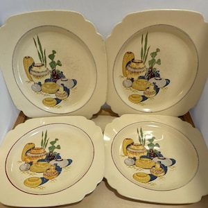 May include: A set of four square cream-colored ceramic plates with rounded corners. Each plate features a central graphic illustration of various pottery vessels in shades of yellow, brown, blue, and green, accented by tall green grass-like stalks.