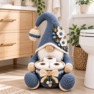 May include: A crocheted gnome figurine in shades of blue and cream, featuring a tall pointed hat adorned with fabric flowers and leaves. The gnome holds a circular basket containing three rolls of toilet paper, accented with a cream bow and button.