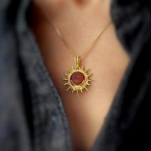 Może przedstawiać: Złoty naszyjnik z zawieszką w kształcie słońca z czerwonym bursztynem w środku.