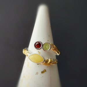 Op de afbeelding: Een zilveren en gouden ring met drie amberstenen. De ring is geplaatst op een witte, kegelvormige displaystandaard.