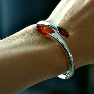 May include: A silver bangle bracelet with two amber stones set into the metal. The bracelet is open and has a hinged clasp.