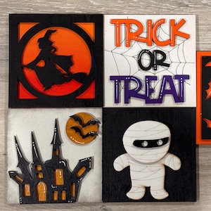 May include: Halloween-themed wooden art pieces. Includes a witch silhouette, the words "Trick or Treat", bats, a mummy, and a haunted house. Each piece is square and features orange, black, white, and purple colors.