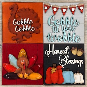 May include: Four square wooden signs with Thanksgiving themes. One sign has a turkey and the words "Gobble Gobble". Another says "Gobble til you wobble". The third sign has a turkey and the fourth says "Harvest Blessings" with pumpkins and acorns.
