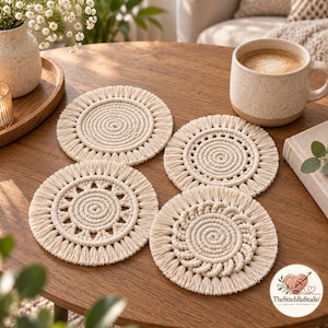 May include: A set of four round, off-white macrame coasters featuring intricate knotted patterns and fringed edges. Each coaster displays a unique circular design, including spiral and geometric motifs, crafted from cotton cord.