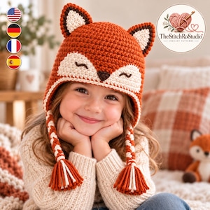 May include: A crochet fox hat featuring a vibrant orange main body with cream-colored accents on the face and ears. The hat includes two braided earflaps ending in tassels, a dark brown nose, and embroidered closed eyes in a sleeping expression.