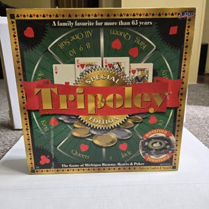 May include: A square board game box for Tripoley Special Edition featuring a green circular play area with playing cards, poker chips, and a rotating turntable graphic. The box has gold borders, red banners, and text including A family favorite for more than 65 years and The Game of Michigan Rummy, Hearts & Poker.