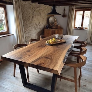 Puede incluir: Una mesa de comedor rectangular con un tablero de madera de borde natural con vetas pronunciadas, sostenida por dos patas de metal negro en forma de U. La mesa está rodeada por seis sillas de madera con respaldos curvos y cojines de asiento claros.