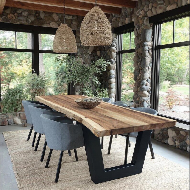 Puede incluir: Una mesa de comedor rectangular con una superficie de madera natural de borde vivo y una base de metal negro en forma de U. Seis sillas grises tapizadas con patas negras est&aacute;n dispuestas alrededor. Dos l&aacute;mparas colgantes tejidas.