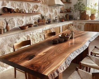 Puede incluir: Una gran mesa de comedor de madera con borde natural, vetas visibles y bordes rugosos. La mesa está rodeada de sillas de madera con asientos tejidos, situada en una cocina con paredes de piedra, estantes de madera y varios cuencos de cerámica.