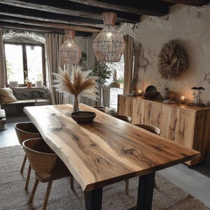 Peut inclure: Une table à manger rectangulaire avec un plateau en bois naturel à bord brut et des pieds en métal noir, entourée de chaises en bois incurvées. Un vase en verre avec de l'herbe de la pampa et un bol sombre sont posés sur la table.