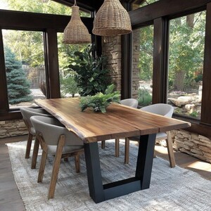 Puede incluir: Una mesa de comedor rectangular con una superficie de madera natural de borde irregular y patas de metal negro en forma de U. Cuatro sillas tapizadas en gris claro con patas de madera rodean la mesa. Dos l&aacute;mparas colgantes de mimbre.