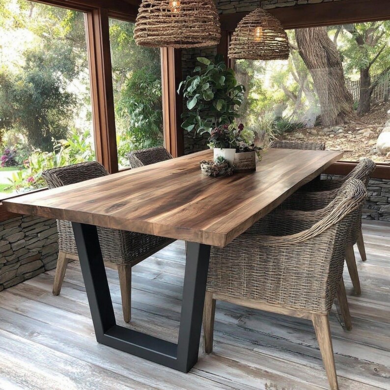 Puede incluir: Una mesa de comedor rectangular de madera con una superficie de grano marr&oacute;n liso y patas de metal negro en forma de U. La mesa est&aacute; rodeada por cuatro sillones de mimbre trenzado y tiene una planta verde en maceta como centro.