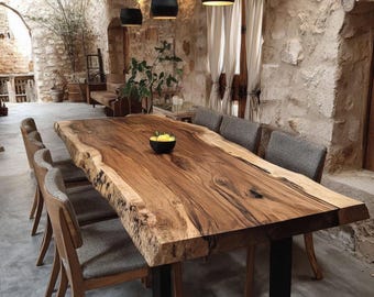 Puede incluir: Una gran mesa de comedor rectangular con un tablero de madera maciza de borde natural, vetas pronunciadas y tonos marrón oscuro, apoyada sobre una base de metal negro en forma de U, acompañada por seis sillas grises tapizadas.