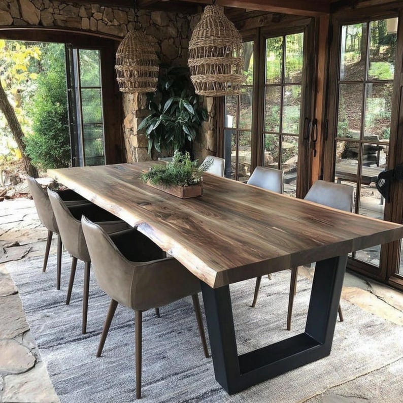 Puede incluir: Una gran mesa de comedor rectangular con una superficie de madera natural de borde vivo y patas de metal negro en forma de U. La mesa est&aacute; rodeada por cuatro sillas tapizadas en gris con patas c&oacute;nicas. Dos l&aacute;mparas colgantes de mimbre cuelgan.