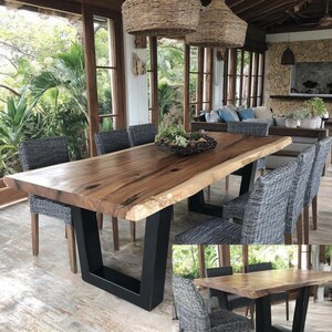Puede incluir: Una mesa de comedor rectangular con una superficie de madera de borde natural y una base de metal negro en forma de U, acompa&ntilde;ada de seis sillas tejidas grises. La mesa presenta un patr&oacute;n de veta de madera marcado y un acabado liso.