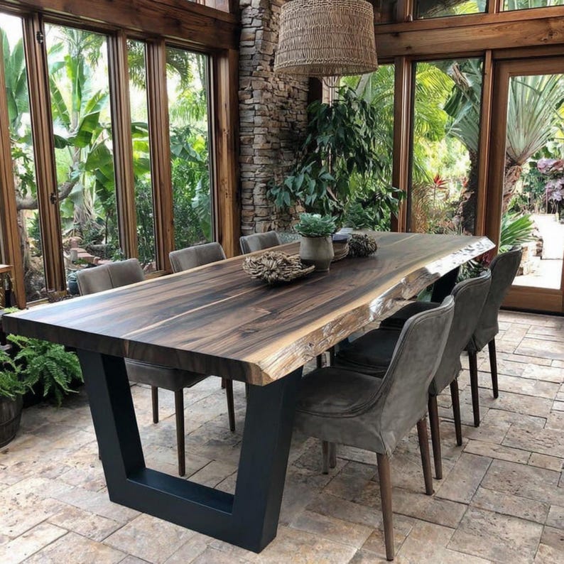 Puede incluir: Una mesa de comedor rectangular con una superficie de madera marr&oacute;n oscuro de borde natural y una base de metal negro en forma de U. La mesa est&aacute; rodeada por seis sillas tapizadas de color gris con patas de madera. Una l&aacute;mpara colgante tejida.