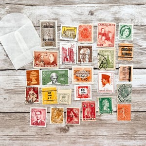 May include: A selection of vintage postage stamps from different nations, showcasing portraits, landmarks, and historical figures. The stamps are displayed on a wooden surface, with a white envelope in the upper left.