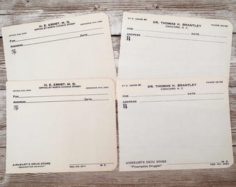 May include: Four blank prescription pads with the names of two doctors, H. E. Ernst, M.D. and Dr. Thomas H. Brantley, and the names of two pharmacies, Airheart's Drug Store and Airheart's Drug Store. The pads are on a wooden surface.