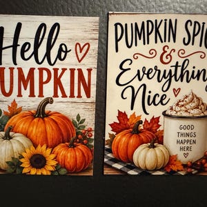 May include: Two rectangular signs featuring autumn themes. The left sign displays the text Hello PUMPKIN with orange pumpkins, a sunflower, and red berries. The right sign displays PUMPKIN SPICE & Everything Nice with a mug and pumpkins.