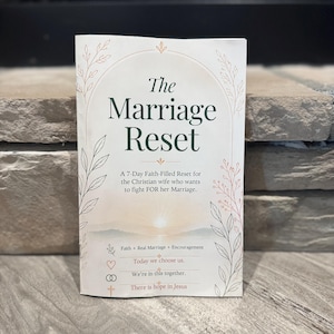 May include: A book titled The Marriage Reset with a subtitle A 7-Day Faith-Filled Reset for the Christian wife who wants to fight FOR her Marriage. The cover features a sunrise illustration, botanical line art, and text including Faith + Real Marriage + Encouragement, Today we choose us, We're in this together, and There is hope in Jesus.