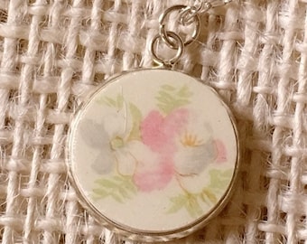 May include: A silver chain necklace with a round pendant featuring a floral design in shades of pink, blue, and green on a white background.