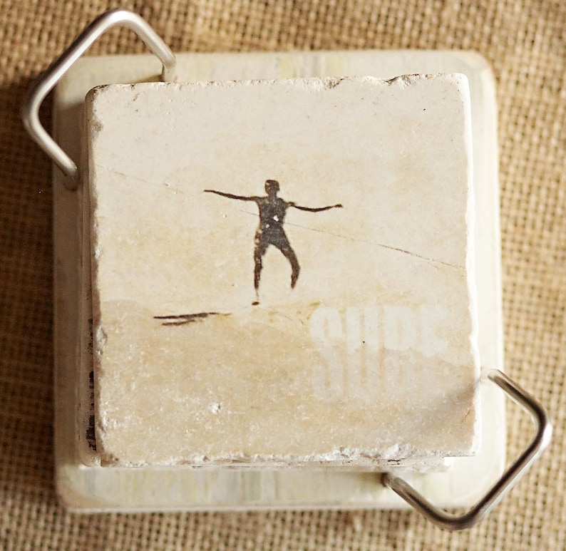 Pode incluir: Um azulejo quadrado branco com uma silhueta preta de uma pessoa com os bra&ccedil;os estendidos. O azulejo est&aacute; em uma moldura de metal com uma al&ccedil;a.