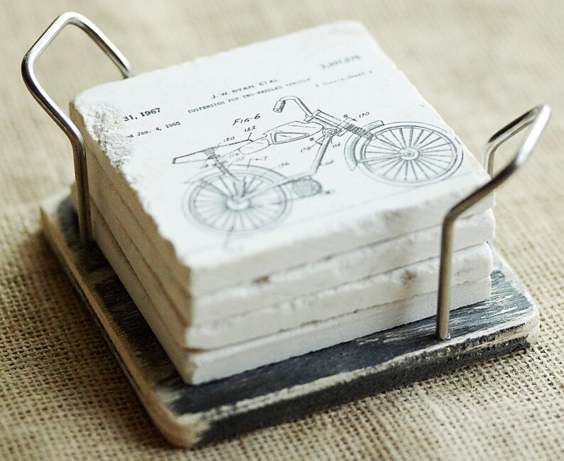 Puede incluir: Conjunto de cuatro posavasos de cer&aacute;mica blanca con un dibujo de patente de motocicleta vintage en blanco y negro. Los posavasos est&aacute;n en un soporte de madera negro con un asa de metal.