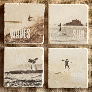 Pode incluir: Conjunto de quatro  tapetes quadrados com tema de praia. Cada tapete apresenta uma imagem diferente: ondas quebrando, um surfista surfando uma onda, palmeiras em uma praia e um surfista com os bra&ccedil;os estendidos. Os tapetes s&atilde;o feitos de pedra bege claro com textura &aacute;spera. As palavras "WAVES", "SUN" e "SHORE" est&atilde;o impressas nos tapetes.