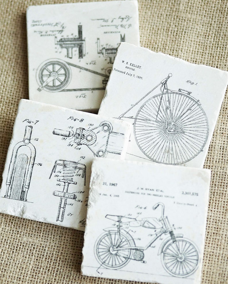Puede incluir: Cuatro dibujos de patentes vintage en azulejos blancos, cada uno representando un dise&ntilde;o de bicicleta diferente. Los dibujos est&aacute;n hechos con tinta negra e incluyen detalles como el cuadro, las ruedas y los engranajes de la bicicleta. Los azulejos est&aacute;n dispuestos en un patr&oacute;n escalonado sobre un fondo de arpillera.