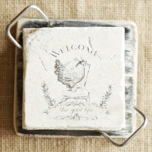 May include: White ceramic coaster with a black and white image of a chicken and the text "Welcome the good life".