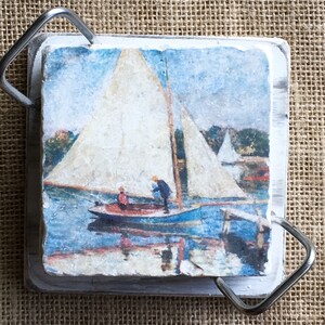 May include: A white wooden coaster with a painted image of a sailboat on a body of water. The coaster has a metal handle on each side.