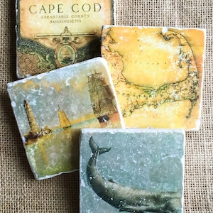 May include: Four square coasters with a nautical theme. The coasters feature images of a lighthouse, a ship, a map of Cape Cod, and a whale. The coasters are made of marble and have a rustic, vintage look.