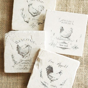 May include: Four square white coasters with black ink designs of roosters and French phrases. The phrases are "Organic Cuisine", "Gourmet Kitchen", "Welcome the good life", and "Bon Appetit mes amis".