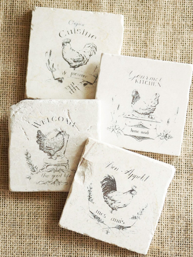 May include: Four square white coasters with black ink designs of roosters and French phrases. The phrases are "Organic Cuisine", "Gourmet Kitchen", "Welcome the good life", and "Bon Appetit mes amis".