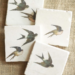 May include: Set of four square coasters with a white background and a vintage illustration of a swallow bird in flight. The coasters are made of natural stone.
